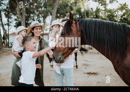 Fröhliche Eltern mit Kindern berühren Pferd, während sie im Freien stehen Stockfoto