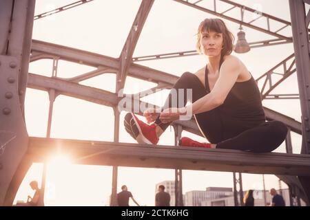 Selbstbewusste Frau beim Sonnenuntergang Schnürsenkel auf Metallbrücke binden Stockfoto