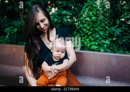 Lächelnde junge Frau mit Baby Junge auf der Bank sitzen parken Stockfoto