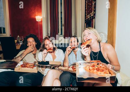 Glückliche Freunde genießen Pizza, während sie auf dem Sofa sitzen während der Party Zu Hause Stockfoto