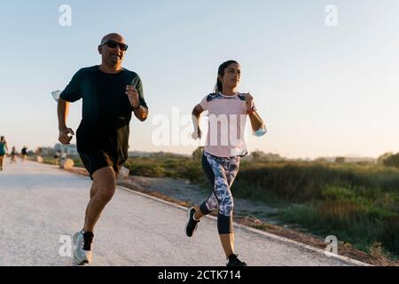 Frau läuft mit Senior Sportler auf der Straße während Sonnenuntergang Stockfoto