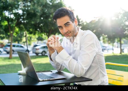 Ein gutaussehender Geschäftsmann mit zusammengekrallten Händen sitzt im Straßencafé Stockfoto