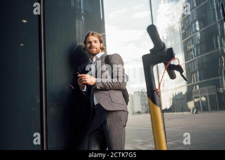 Männliche professionelle lehnt auf Glas durch elektrische Push-Roller an Innenstadt Stockfoto