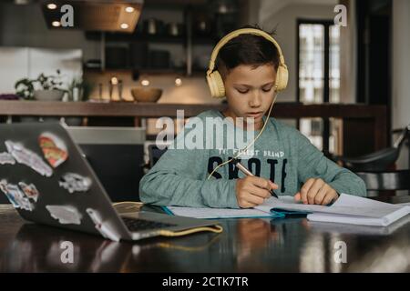 Schuljunge zu Hause lernen, mit Laptop und Kopfhörer Stockfoto