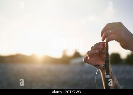 Hände eines mittleren erwachsenen Mannes, der Angelrute am Strand vorbereitet Gegen den Himmel bei Sonnenuntergang Stockfoto