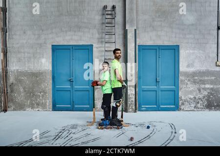 Vater und Sohn stehen zurück an den Rücken, während sie Hockey halten Stöcke an den Türen am Hof Stockfoto