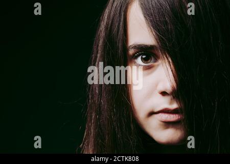 Nahaufnahme des Mädchens mit langen braunen Haaren im Gesicht gegen Schwarzer Hintergrund Stockfoto