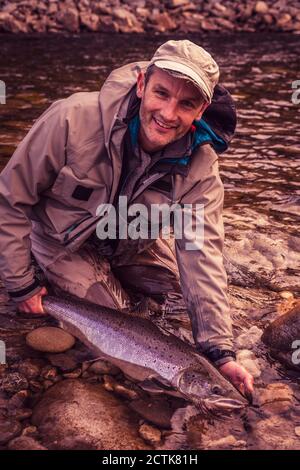 Lächelnder Fliegenfischer hält gefangenen Lachsfisch im Fluss Stockfoto