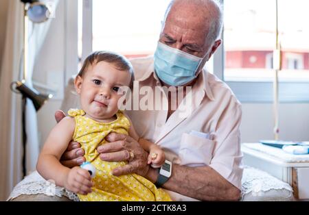 Großvater mit Schutzmaske und Baby-Mädchen zu Hause Stockfoto