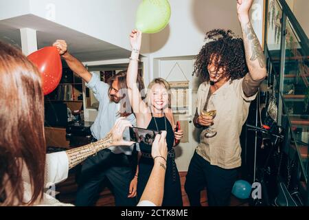 Frau fotografiert glückliche Freunde tanzen während der gesellschaftlichen Zusammenkunft zu Hause Stockfoto