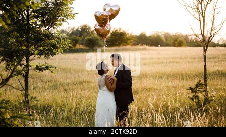 Brautpaar hält Herz-Form Helium Ballons, während im Stehen Feld bei Sonnenuntergang Stockfoto