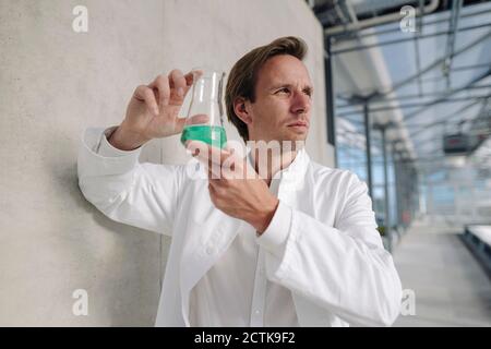 Wissenschaftler hält Becher mit Flüssigkeit an einer Wand Stockfoto