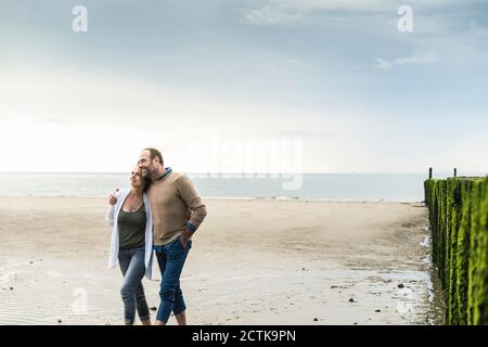 Liebevolles reifes Paar, das am Strand gegen Meer während des Sonnenuntergangs läuft Stockfoto