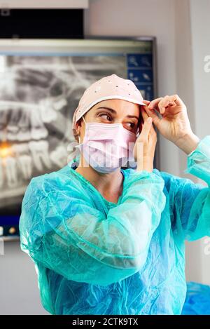 Zahnarzt im Schutzanzug mit OP-Kappe während des Stehens Klinik Stockfoto