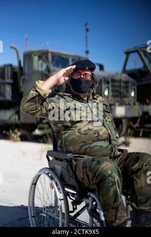 Militäroffizier salutieren, während er auf dem Rollstuhl gegen LKW sitzt Stockfoto