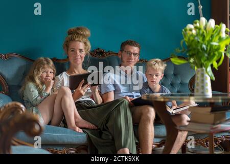 Familiensitting mit digitalem Tablet und Fotoalbum auf Sofa Im Wohnzimmer Stockfoto