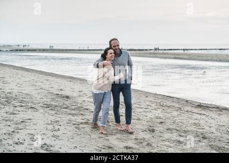 Ein glückliches Paar umarmte sich beim Spaziergang am Strand während des Sonnenuntergangs Stockfoto