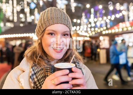 Nahaufnahme der glücklichen schönen Frau hält heiße Schokolade in Weihnachten Markt bei Nacht Stockfoto