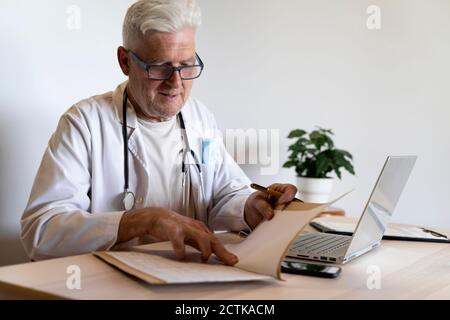 Leitender Arzt, der in der Klinik sitzt und die Krankenakte betrachtet Stockfoto