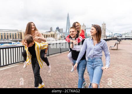 Männliche Freunde Huckepack weibliche Freunde beim Spaziergang auf dem Fußweg in der Stadt, London, Großbritannien Stockfoto