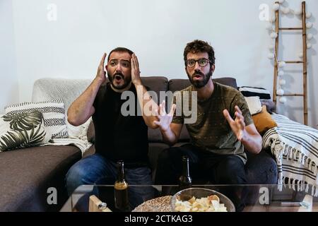 Gestresste männliche Freunde beobachten Sport, während sie auf dem Sofa sitzen Zu Hause Stockfoto