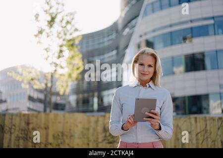 Selbstbewusste Geschäftsfrau hält digitale Tablet, während sie gegen Gebäude an Finanzviertel Stockfoto