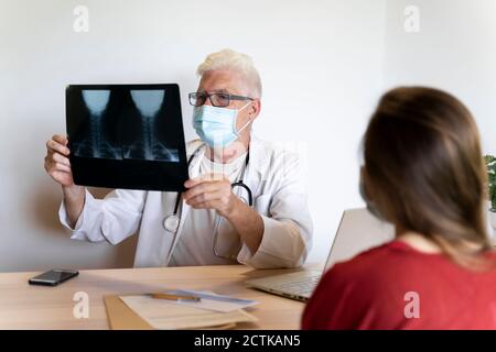 Arzt, der jungen Patienten Ratschläge gibt, während er medizinische Röntgenaufnahmen analysiert Stockfoto
