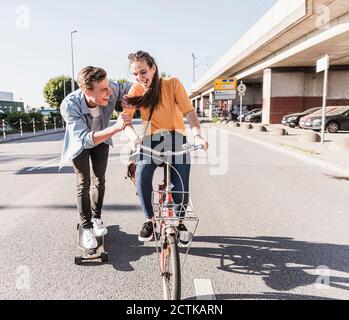 Verspielt Freund Skateboarding während Freundin Fahrrad auf der Straße in Stadt Stockfoto