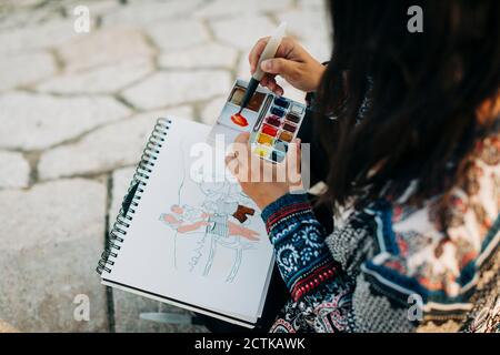 Frau malen mit Aquarell, während sie am Fußweg sitzt Stockfoto