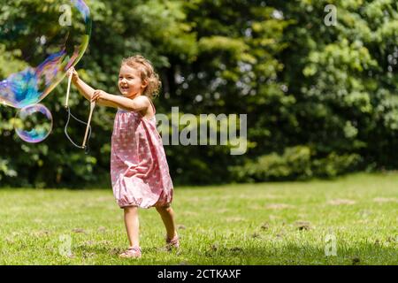 Lächelndes Mädchen läuft mit Bubble Zauberstab im Park Stockfoto