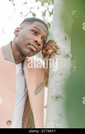 Nachdenklicher junger Mann, der sich auf einen Baum stützt Stockfoto