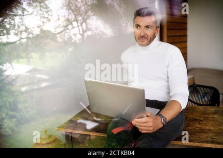 Durchdachter Manager mit Laptop auf dem Schreibtisch im Büro gesehen Durchgangsfenster Stockfoto