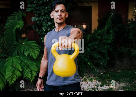 Mid adult man Heben Kettlebell, während gegen Pflanzen in stehen Hof Stockfoto