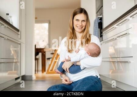 Blonde Frau hält schlafen Baby junge, während auf dem Boden sitzen Zu Hause Stockfoto