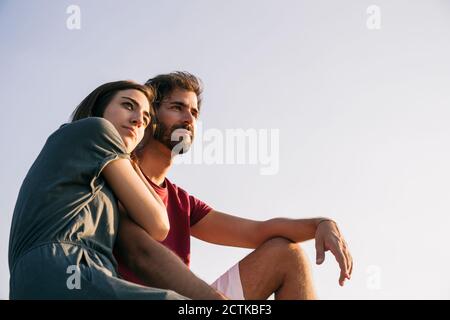 Junge Frau lehnte sich auf Mann Schulter, während sie gegen klar sitzt Himmel Stockfoto