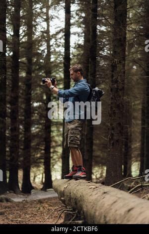 Männlicher Wanderer, der mit der Kamera fotografiert, während er auf der Anmeldung steht Waldgebiet Stockfoto