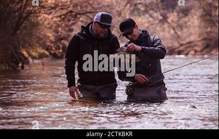 Fischer und Sohn halten gefangenen Fisch, während sie im Fluss stehen Im Wald Stockfoto