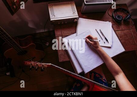 Junge Frau, die im Buch schreibt, während sie zu Hause Gitarre übt Stockfoto