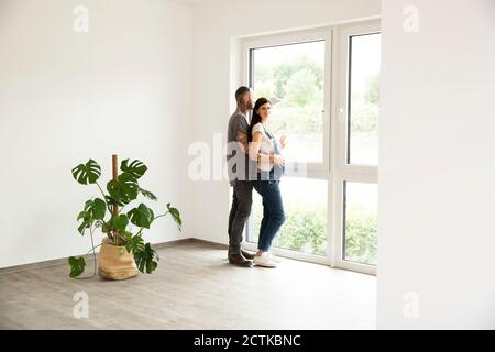 Schwangere Frau steht mit Mann durch Fenster in neu schauen Zu Hause Stockfoto