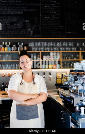 Lächelnde Unternehmerin mit gekreuzten Armen, die im Café stehen Stockfoto