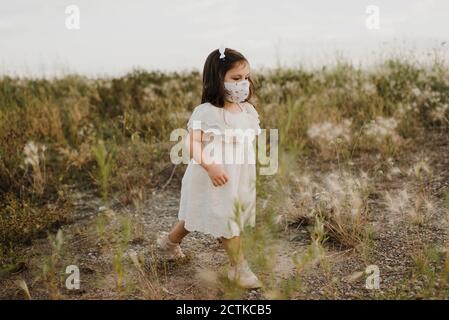 Nettes Mädchen tragen schützende Gesichtsmaske zu Fuß im Feld Stockfoto