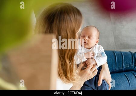 Blonde Frau hält schlafenden Jungen in den Armen während des Sitzens Auf dem Boden zu Hause Stockfoto