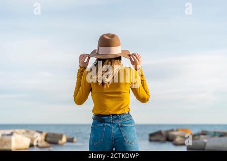 Junge Frau mit Sonnenhut, während sie gegen das Meer steht Stockfoto