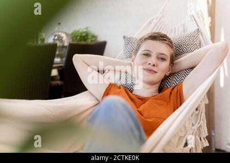 Lächelnde schöne Frau mit Händen hinter dem Kopf, die auf Hängematte ruhen Auf der Veranda Stockfoto