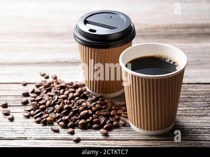 Eine Papiertasse mit Kaffee und Kaffeebohnen auf einem Alter Holzhintergrund Stockfoto