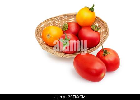 Eine Gruppe von gelben und roten Tomaten in einem Strohkorb, isoliert auf einem weißen Hintergrund. Stockfoto