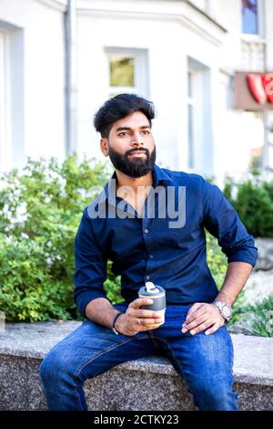 Junger indischer Mann trinkt Kaffee aus wiederverwendbarer Tasse im Freien. Stockfoto