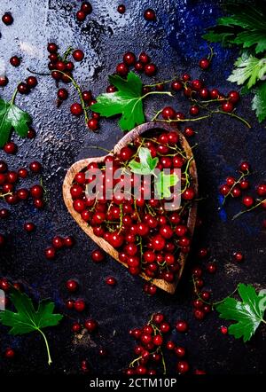 Rote Johannisbeeren in Schale in Herzform, Futterhintergrund, Draufsicht Stockfoto