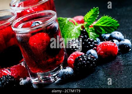 Kalter Sommerbeerentee mit Himbeeren, Heidelbeeren, Brombeeren und Minze in Gläsern auf dunklem Hintergrund, selektiver Fokus Stockfoto