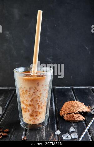 Eiskaffee im Thai-Stil mit Kokosmilch und Kaffeebohnen auf schwarzem Holzhintergrund. Stockfoto